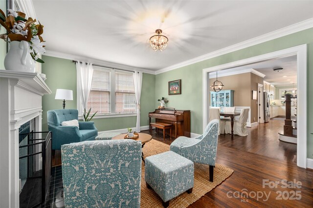 living area featuring a chandelier, wood finished floors, crown molding, baseboards, and a fireplace