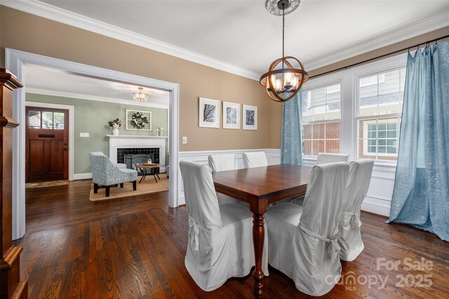 dining area with a chandelier, ornamental molding, healthy amount of natural light, dark wood-type flooring, and a wainscoted wall