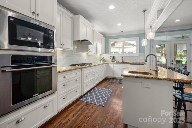 kitchen with appliances with stainless steel finishes, a sink, ornamental molding, a kitchen bar, and french doors