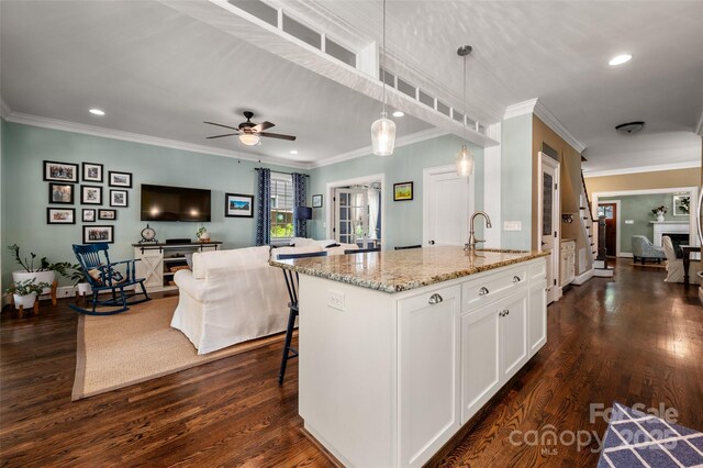 kitchen with a sink, light stone counters, white cabinetry, ornamental molding, and decorative light fixtures