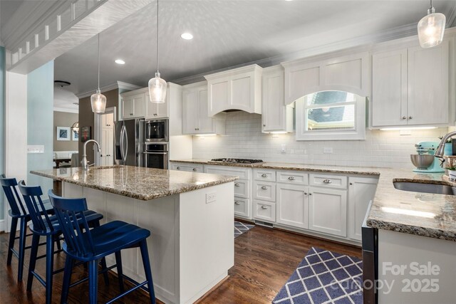 kitchen with a sink, appliances with stainless steel finishes, white cabinets, ornamental molding, and recessed lighting