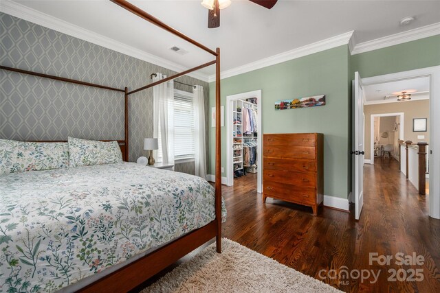 bedroom featuring baseboards, a walk in closet, wood finished floors, ornamental molding, and a closet