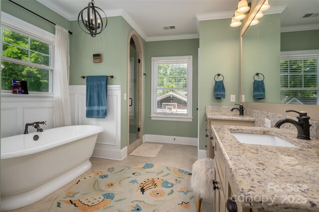 bathroom featuring a chandelier, healthy amount of natural light, ornamental molding, a soaking tub, and double vanity