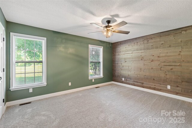carpeted empty room with a textured ceiling, ceiling fan, wooden walls, and baseboards