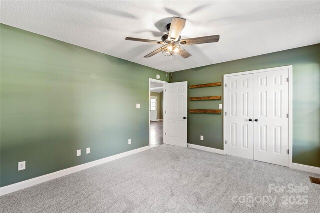 unfurnished bedroom with carpet floors, baseboards, a textured ceiling, ceiling fan, and two closets