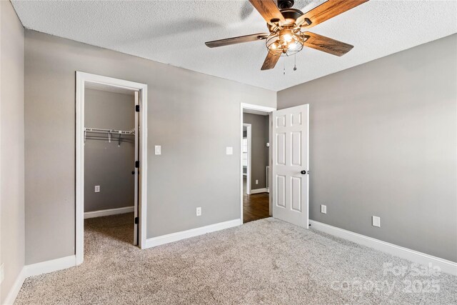 unfurnished bedroom featuring carpet, a spacious closet, a textured ceiling, baseboards, and a closet