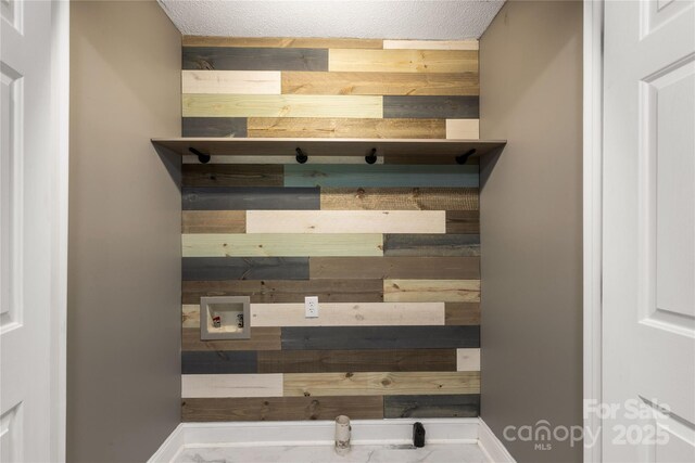 laundry view of wooden walls, a textured ceiling, and baseboards