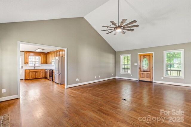 unfurnished living room with high vaulted ceiling, ceiling fan, baseboards, and wood finished floors