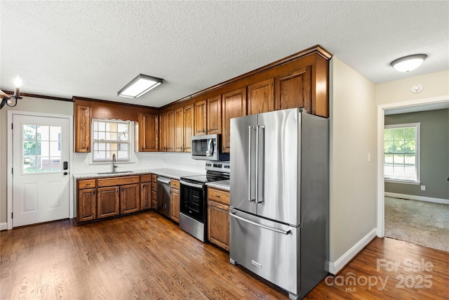 kitchen with stainless steel appliances, a sink, brown cabinets, a textured ceiling, and dark wood finished floors