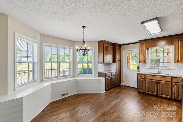 kitchen with a sink, a chandelier, tasteful backsplash, dark wood-style floors, and a textured ceiling