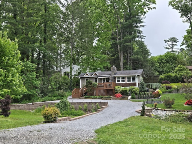 view of front facade featuring a chimney, driveway, a deck, and a front yard