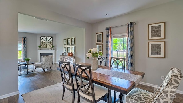 dining area featuring baseboards, a fireplace, visible vents, and dark wood-type flooring