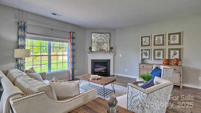 living area with wood finished floors, visible vents, baseboards, and a fireplace with flush hearth