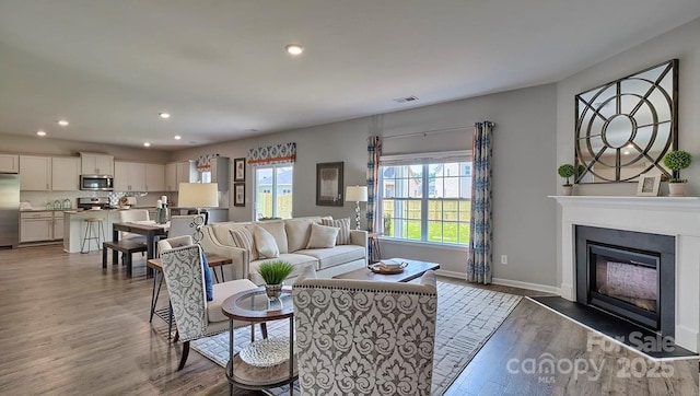 living area with light wood-style flooring, visible vents, baseboards, a glass covered fireplace, and recessed lighting