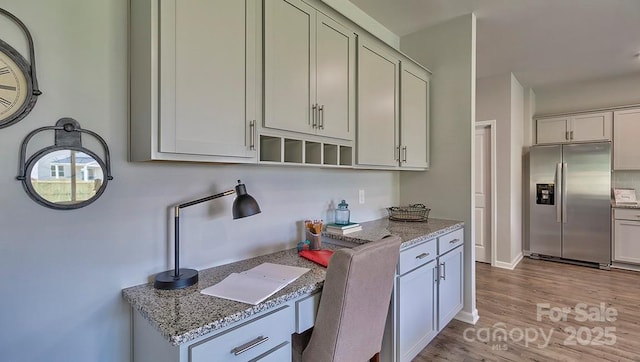 kitchen featuring built in desk, light stone countertops, stainless steel fridge, and light wood-style floors