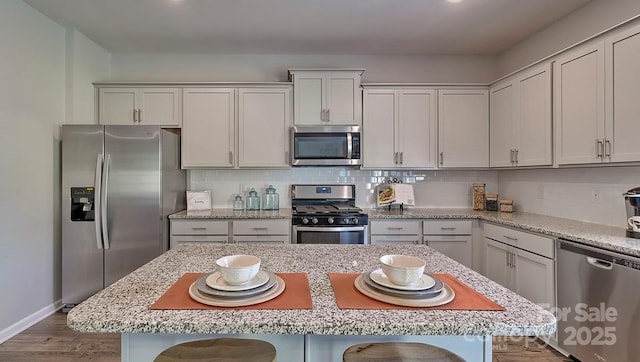 kitchen with a breakfast bar area, baseboards, wood finished floors, backsplash, and appliances with stainless steel finishes