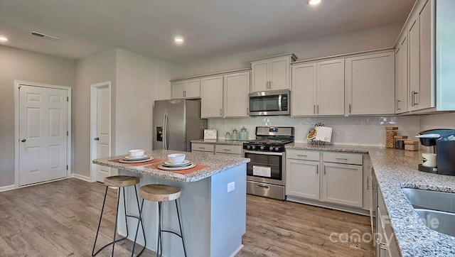 kitchen featuring stainless steel appliances, visible vents, light wood-style flooring, a kitchen bar, and a kitchen island