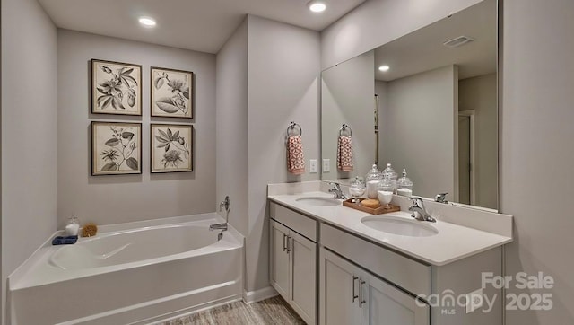 full bathroom with a garden tub, double vanity, a sink, and wood finished floors
