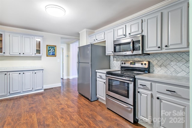 kitchen featuring appliances with stainless steel finishes, light countertops, decorative backsplash, glass insert cabinets, and dark wood finished floors