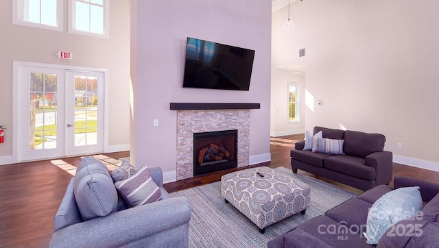 living room with french doors, baseboards, a stone fireplace, a towering ceiling, and wood finished floors