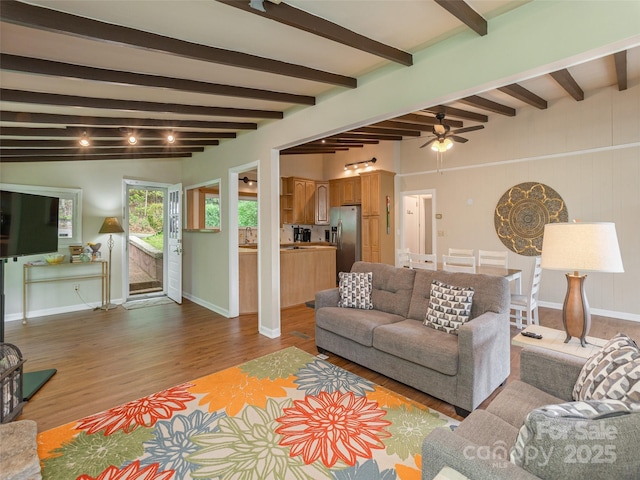 living area with wood finished floors, a ceiling fan, baseboards, and beamed ceiling
