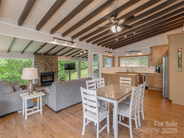 dining room with track lighting, a stone fireplace, healthy amount of natural light, and ceiling fan
