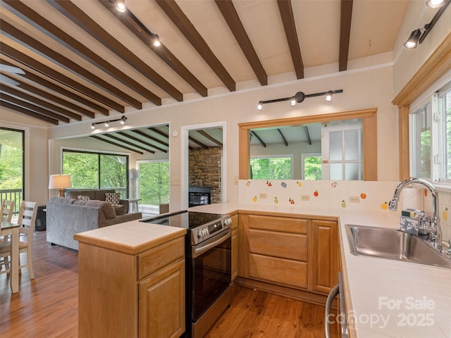 kitchen with electric range, a sink, tile counters, open floor plan, and light wood finished floors