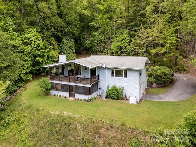 back of house with a chimney, a forest view, a yard, a sunroom, and roof with shingles