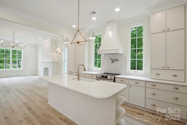kitchen featuring premium range hood, a sink, a chandelier, stainless steel range with electric stovetop, and light wood-style flooring