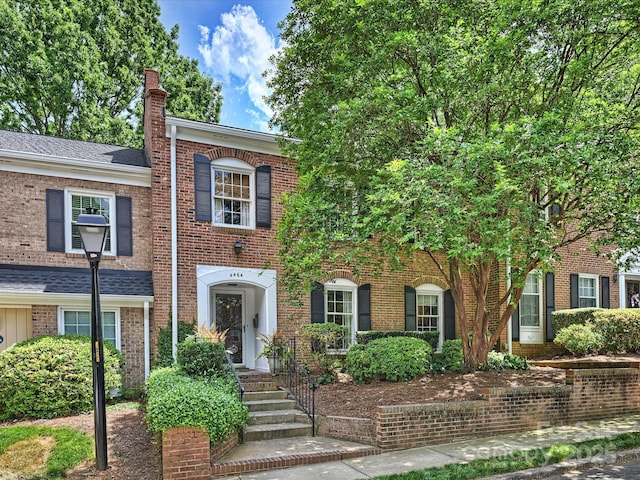 view of front of home with a chimney, brick siding, and a shingled roof