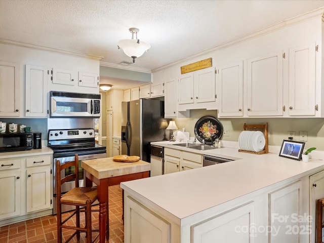kitchen with stainless steel appliances, brick patterned floors, light countertops, crown molding, and a peninsula