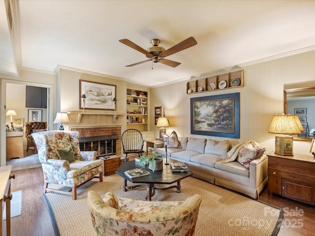 living room featuring ornamental molding, wood finished floors, a ceiling fan, a fireplace, and built in features