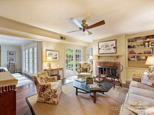 living area featuring ornamental molding, ceiling fan, a brick fireplace, wood finished floors, and a textured ceiling