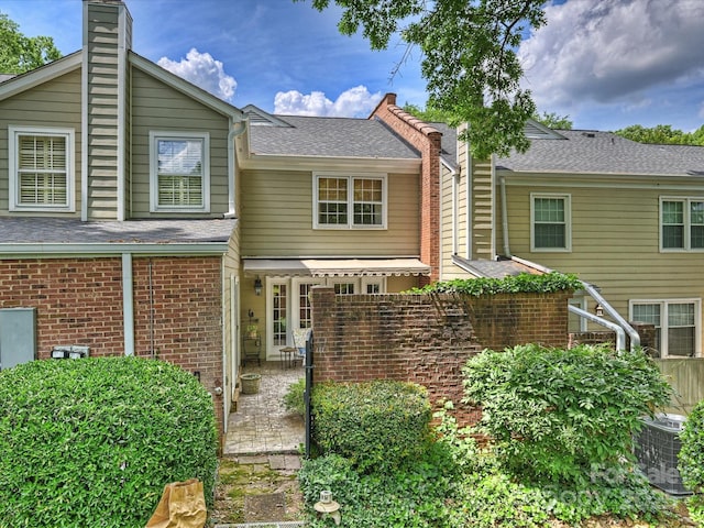 view of front of house featuring cooling unit, brick siding, a chimney, and a patio area