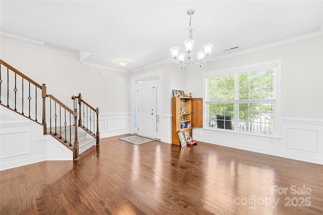 foyer entrance with stairway, a chandelier, wood finished floors, wainscoting, and ornamental molding