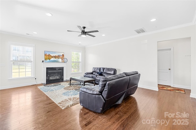 living area with wood finished floors, a ceiling fan, a glass covered fireplace, crown molding, and baseboards
