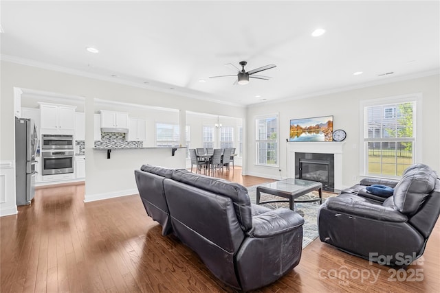 living area featuring a ceiling fan, ornamental molding, recessed lighting, hardwood / wood-style flooring, and a glass covered fireplace