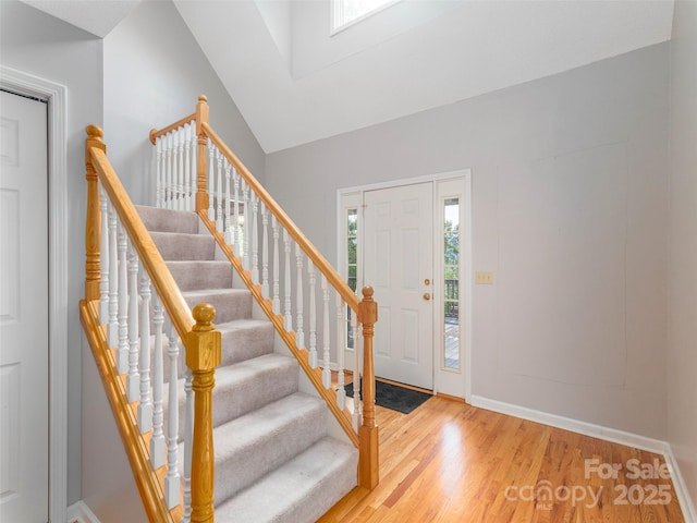 foyer entrance with vaulted ceiling, stairway, wood finished floors, and baseboards