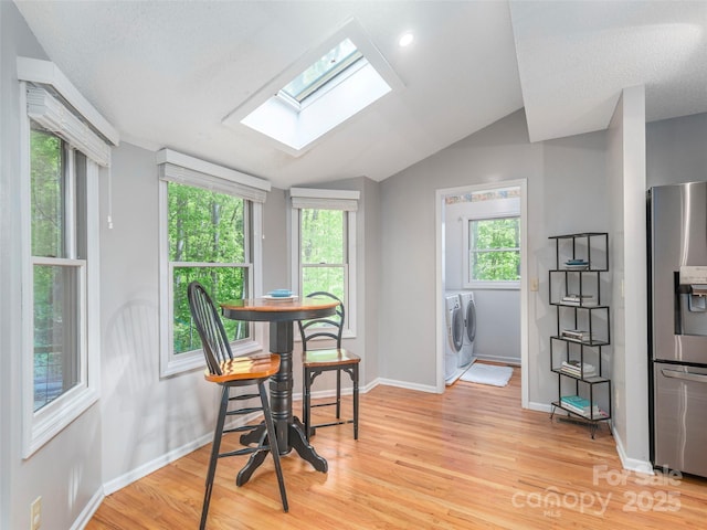 dining space featuring baseboards, light wood-style flooring, vaulted ceiling with skylight, and washer and clothes dryer