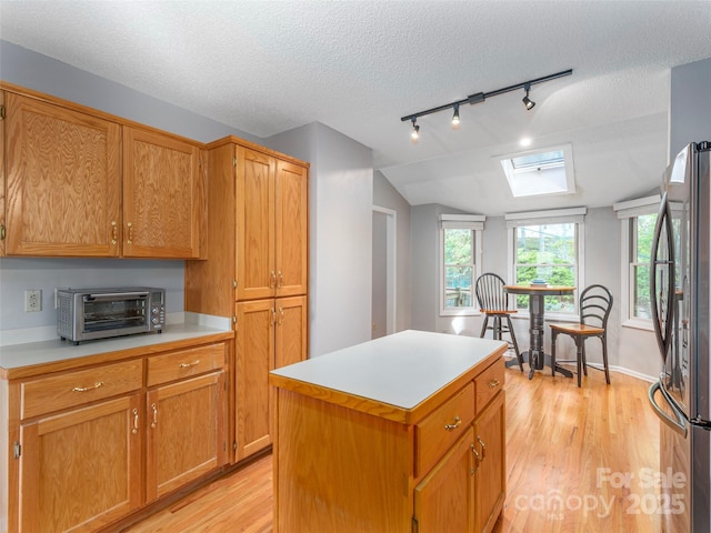 kitchen with freestanding refrigerator, track lighting, a toaster, light countertops, and light wood-style floors