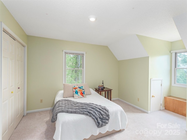 bedroom featuring a closet, baseboards, light colored carpet, lofted ceiling, and radiator heating unit