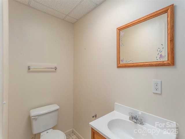 half bath featuring toilet, baseboards, tile patterned floors, vanity, and a paneled ceiling