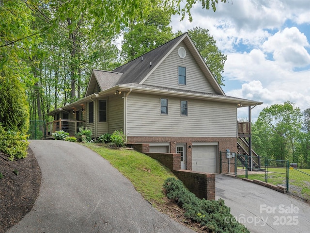 view of home's exterior with an attached garage, covered porch, stairway, brick siding, and driveway