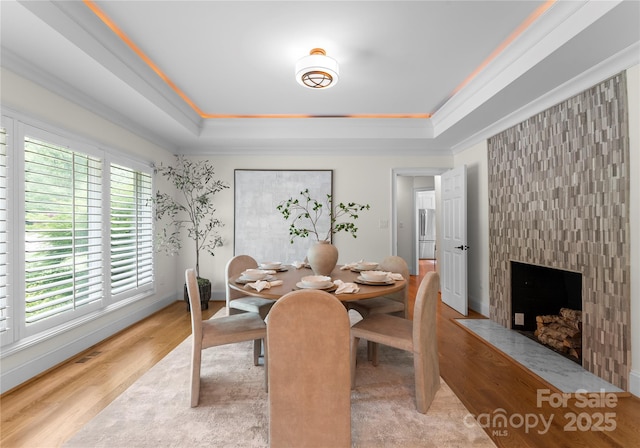 8300 Fairview Rd, Charlotte, NC 28226 - dining room featuring a raised ceiling, light wood-style floors, baseboards, crown molding, and a fireplace