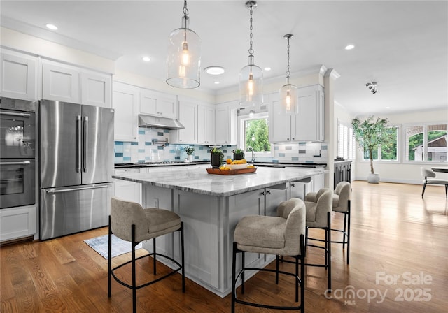 8300 Fairview Rd, Charlotte, NC 28226 - kitchen with appliances with stainless steel finishes, under cabinet range hood, tasteful backsplash, wood finished floors, and white cabinetry