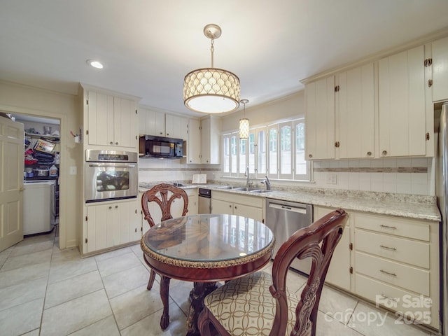 kitchen with a sink, pendant lighting, backsplash, washer / dryer, and appliances with stainless steel finishes