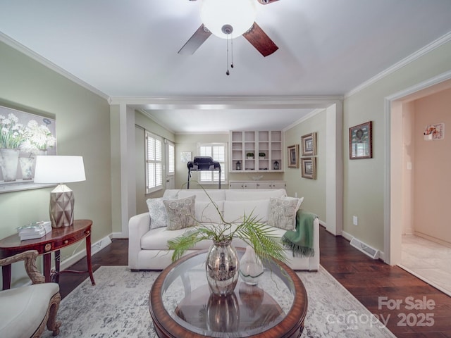 living room featuring a ceiling fan, visible vents, baseboards, dark wood-style flooring, and ornamental molding