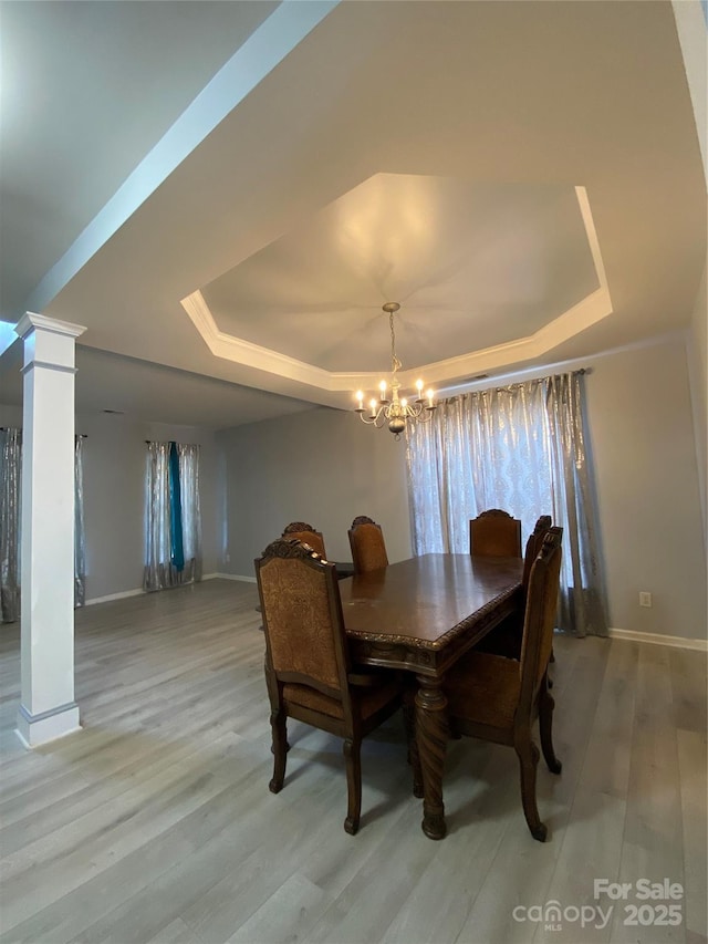 dining space with a tray ceiling, light wood-type flooring, a chandelier, and decorative columns
