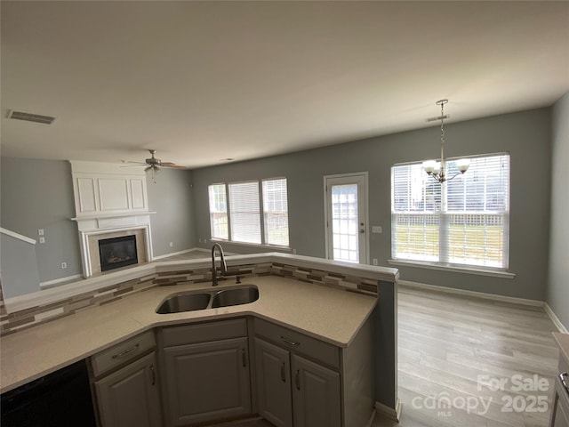 kitchen with ceiling fan with notable chandelier, a sink, open floor plan, visible vents, and light countertops