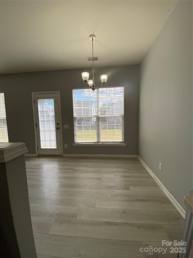 unfurnished dining area with light wood-type flooring, a wealth of natural light, an inviting chandelier, and visible vents